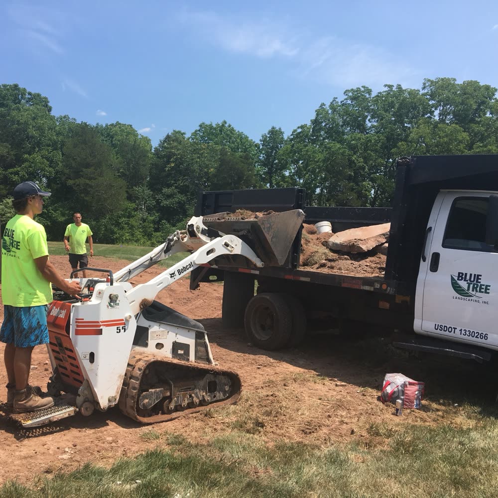 Blue Tree crew loading a skid steer on a job site.